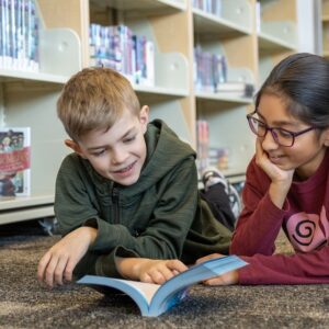 Two students reading a book together in a library