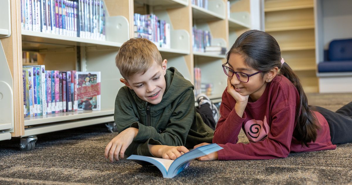 Two students reading a book together in a library